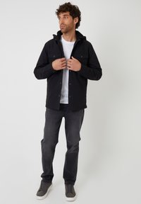 Czarna kurtka z kapturem z frontowymi guzikami, dwiema kieszeniami na piersi i miękką podszewką. Połączona z ciemnymi dżinsami i szarymi trampkami. Pod spodem zwykła biała koszula.