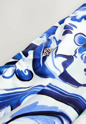 Blau-weiß gemusteter Stoff mit Wirbeln, an dem ein kleiner goldener runder Knopf befestigt ist. Glatte Textur, leichtes Material.