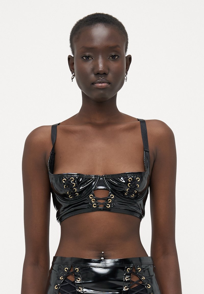 Crop top iz črnega lakiranega usnja z nastavljivimi naramnicami, nabrano obliko, zlatimi očesci in izrezom na sprednjem delu.