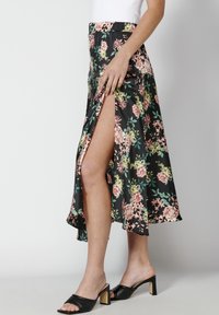 Musta satiininen kukallinen midi-hame, jossa on korkea halkio ja kirkkaan pinkkejä ja vihreitä kukkakuvioita. Yhdistetty mustiin korkokenkiin.