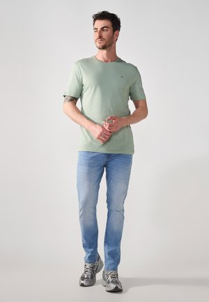 Lys grøn t-skjorte i bomull med korte ermer, sammen med lyseblå denimbukser. Grå joggesko med sølvdetaljer fullfører antrekket.