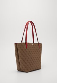 Hnědá taška na rameno s vzorem a červenými syntetickými koženými držadly. Má robustní tvar a otevřenou horní část, která odhaluje prostorný interiér.