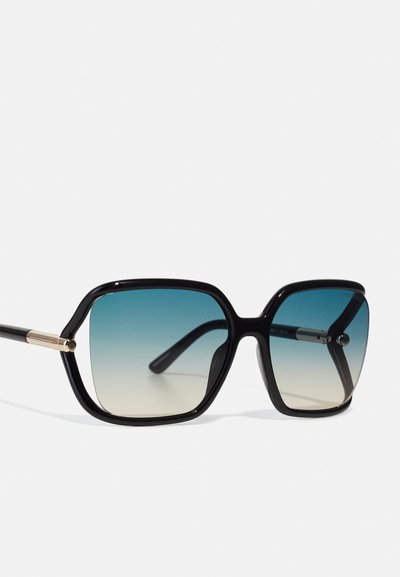 Occhiali da sole oversize neri con lenti sfumate da blu a beige chiaro. Presentano una montatura spessa con dettagli dorati e aste nere sottili.