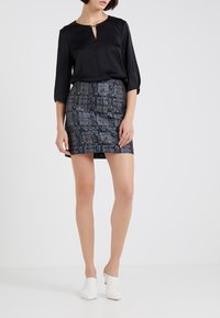 Blouse noire avec un décolleté en trou de serrure et des manches trois-quarts, assortie à une jupe moulante avec un motif géométrique bleu et blanc. Mules blanches.