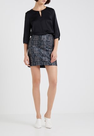 Blouse noire avec un décolleté en trou de serrure et des manches trois-quarts, assortie à une jupe moulante avec un motif géométrique bleu et blanc. Mules blanches.