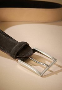 Barna velúr öv ezüst téglalap csattal, varrott szélekkel és sima felülettel, egy bézs háttéren fekszik.