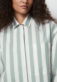 Camisa a rayas verde claro y blanca con cuello, cierre de botones y un bolsillo en el lado izquierdo. Tejido suave con un ajuste relajado.
