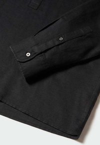 Puño de camisa de manga larga negra con dos botones visibles sobre un fondo de tela suave.