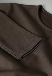 Vêtement marron foncé à manches longues avec des coutures visibles autour des poignets et du col, fabriqué en tissu lisse et épais.