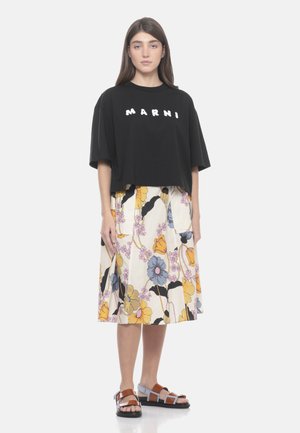 Donna che indossa una t-shirt nera Marni, gonna floreale al ginocchio gialla, blu e rosa, e sandali open-toe con cinturini marroni e blu.