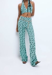 Two-piece outfit featuring a halter top and flared pants in green with a zigzag pattern. The pants have a chain accent at the waist.