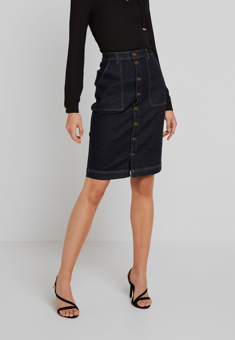 Jeanskjol med hög midja, mörkblå tvätt, knäppningar fram och två framfickor. Parat med en figurnära svart tröja med långa ärmar.