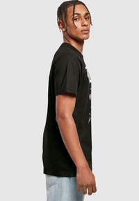 Juodas medvilnės marškinėliai su apvalia iškirpte, priekyje turi grafišką spaudą. Dėvimi su šviesiais džinsais, atskleidžiantys laisvą siluetą.