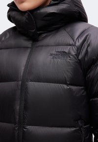 Άτομο που φοράει μαύρο επενδυμένο μπουφάν The North Face με ψηλό γιακά και μπροστινό φερμουάρ, κοντινή λήψη στην περιοχή του στήθους και του λαιμού.
