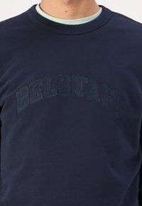 Felpa blu navy realizzata in cotone. Presenta la scritta in rilievo "BELSTAFF" con un filo di contrasto sul petto. Design classico a collo rotondo.