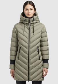 Puffa-jacka i olivgrön med chevron-quilting, hög huva, framsida med blixtlås och två sidfickor med svarta blixtlåsdetaljer.