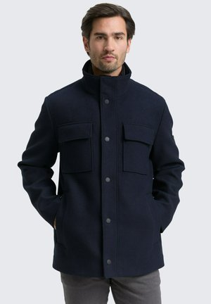 Marineblaue Wollmischjacke mit hohem Kragen, vier Fronttaschen und Druckknöpfen. Sie verfügt über ein strukturiertes Design und eine glatte Textur.