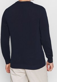 Tyrkysově modrý pletený svetr s dlouhými rukávy, žebrovanými manžetami a spodním lemem. Má kulatý výstřih a hladkou texturu. Zobrazeno zezadu.