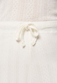 Haut en tissu blanc avec des rayures texturées et de petits motifs en diamant ; présente une taille avec un nœud noué.