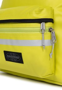 Sac à dos Eastpak jaune avec une poche zippée à l'avant, une bande réfléchissante et un tissu texturé avec un patch logo noir.