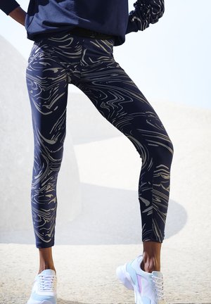 Navy leggings with a gold wavy pattern, featuring a high waist and stretchy material. Paired with light sneakers.