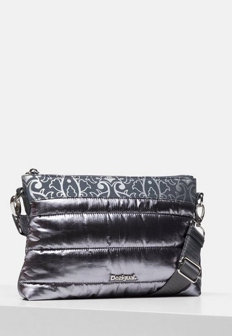 Wypukła metaliczna srebrna torba z szarym wzorzystym materiałowym wierzchem, regulowanym paskiem i zamkiem błyskawicznym. Na przodzie znajduje się logo "Desigual".