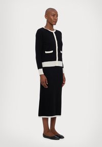 Black knit dress with white accents. Features a round neckline, button front, and two front pockets. Long sleeves and a mid-length silhouette.