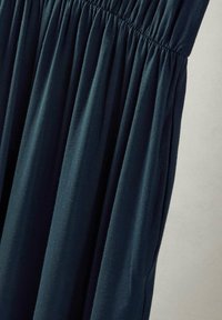 Sukienka w ciemnozielonym kolorze, z elastycznym pasem, wykonana z miękkiego materiału. Posiada zmarszczoną fakturę, zwiewny kształt oraz boczne kieszenie dla dodatkowej funkcjonalności.