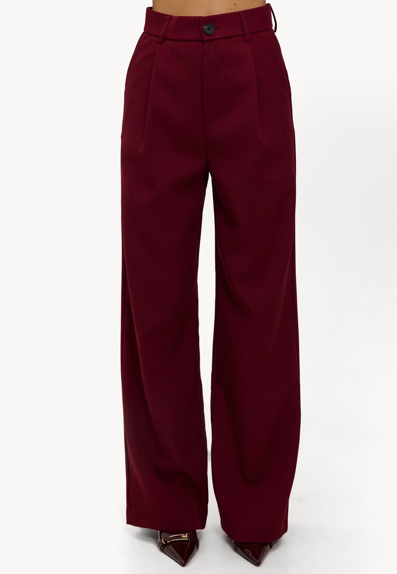 Pantalon large bordeaux taille haute, avec plis à l'avant et fermeture par un seul bouton. Confectionné dans un tissu lisse.