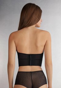 Zwarte strapless korsettop met een gladde textuur, met een doorschijnend middenstuk en een haaksluiting op de rug, gecombineerd met doorschijnende zwarte shorts.