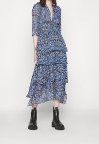 Vestido azul estampado con diseño cruzado, volante en capas y mangas 3/4. Combina con botines negros de tacón ancho.