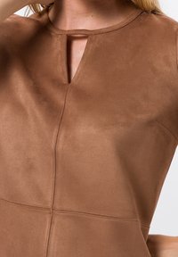 Haut marron à texture douce avec un décolleté en forme de serrure, des détails cousus et une finition lisse. Design simple et moderne sans motifs ni embellissements.