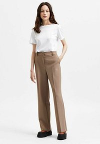 Beige op maat gemaakte broeken met een uitlopende silhouette, met een gladde textuur en zijzakken, gecombineerd met een simpele witte T-shirt en zwarte platform schoenen.