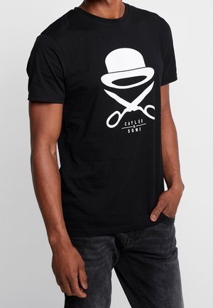 Mężczyzna w czarnej koszulce z białym nadrukiem melonika nad skrzyżowanymi nożyczkami oraz tekstem "Cayler & Sons".