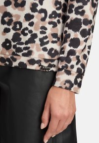 Sweter w panterkę z teksturą prążkowaną, beżowym tłem, czarnymi akcentami i detalem ze sznurkiem na dole. Pod spodem czarne skórzane spodnie.