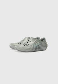 Green plastic slip-on clogs with multiple ventilation holes, wave-like texture, and a small blue Nike logo on the side.