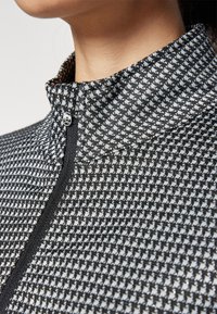 Black and white patterned quarter-zip top with a high collar. Features a soft texture and subtle metallic sheen near the zip closure.