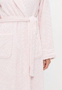 Rosa fluffig badrock med diamantmönster, som har ett bälte, två framfickor och uppvikta ärmar. Mjuk textur och avslappnad passform.