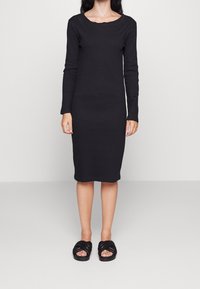 Zwart geribbelde gebreide jurk met lange mouwen, ronde hals en slim fit, gecombineerd met zwarte geweven instapsandalen. Zachte textuur, knielengte.