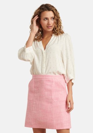 White blouse with subtle patterns and elastic cuffed sleeves, paired with a textured pink skirt featuring two front pockets.
