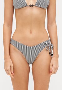 Čierny a biely pruhovaný bikiny top s trojuholníkovými pohárikmi a korálikovým doplnkom. Zodpovedajúce nízko zvýšené bikiny spodky so bočnými viazaniami a detailom loga.