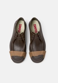 Scarpe in pelle marrone con punta in gomma color tan, forma rotonda e design con lacci. L'interno presenta il marchio rosso "CAMPER" su una soletta testurizzata.