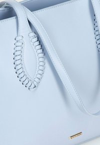 Sac fourre-tout en cuir bleu clair avec des accents de poignées tressées et une petite plaque logo dorée. Texture lisse avec un design structuré.
