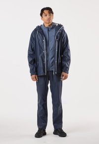 Laivaston sininen vedenpitävä takki hupulla, vetoketjullinen edestä ja joustovarsilla, päällystetty vaaleansinisellä fleecellä, yhdistetty samansävyisiin housuihin.