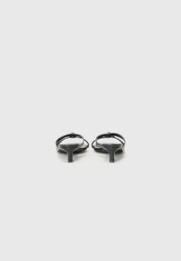 Des sandales noires à talons avec des lanières fines, des pointes effilées et un petit talon carré, présentant une finition brillante sans motifs ni accents visibles.