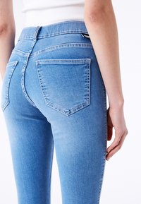 Jeans de color azul claro vistos desde un ángulo cercano, con un diseño ajustado, bolsillos traseros con detalles de costura y una textura de denim suave.
