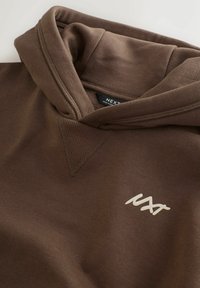 Brązowa hoodie z przednią kieszenią kangurką, kapturem ze sznurkiem i białym logo. Gładki materiał z prążkowanym dekoltem i akcentami na ramionach.