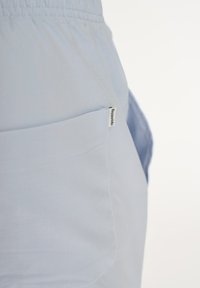 Lyseblå stofshorts med elastrisk talje og en sidelomme med et lille mærkat. Glat tekstur, afslappet pasform.