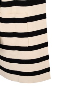 Prenda de lana con rayas horizontales en negro y crema, que cuenta con un bolsillo lateral y una textura suave. Bordes limpios con un corte relajado.
