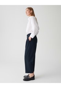 Witte overhemd met knopen, marineblauwe hoge taille broek en zwarte instapschoenen. Glad fabric met een getailleerde pasvorm en zijzakken.